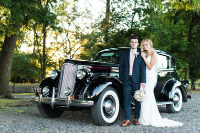 Bride and groom standing next to an antique car