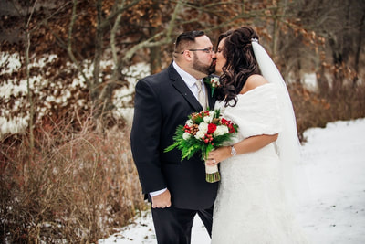 Bride and groom kissing and posing in snow with bouquet