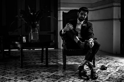 Black and white photo of groom getting his shoes on preparing for the wedding