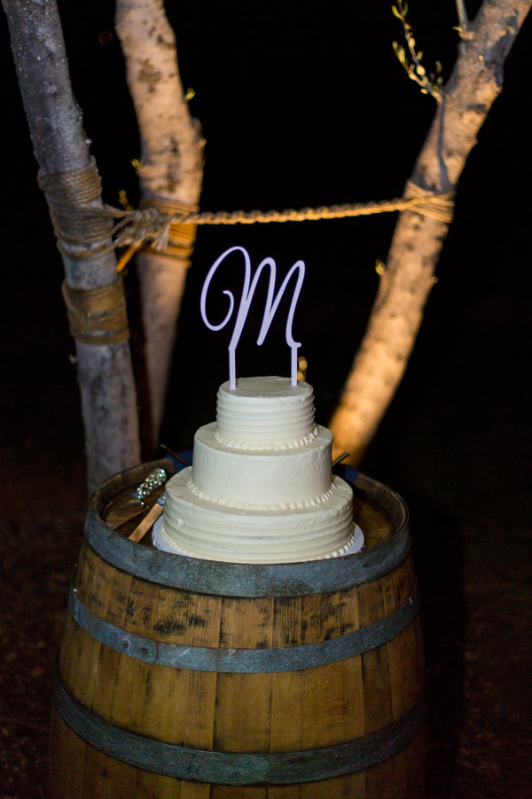 Tiered wedding cake with an M topper sitting ontop of a cask